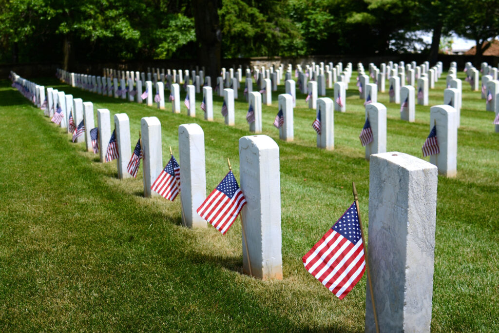 American Flags on the graves of USA War Veterans. Rows of grave stones in a National cemetery decorated with American flags for Memorial Day. Honoring our war dead veterans by placing flags on their tombs.